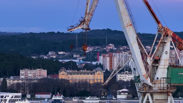 Aerial view of rusty cranes looming over the still harbor waters, contrasting with the urban skyline of the city, Pula, Istria County, Croatia.