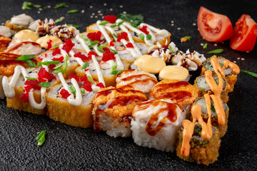 Assorted sushi rolls platter with red tobiko, spicy sauce, creamy topping and crispy maki on dark stone background © Александр Гаврилычев