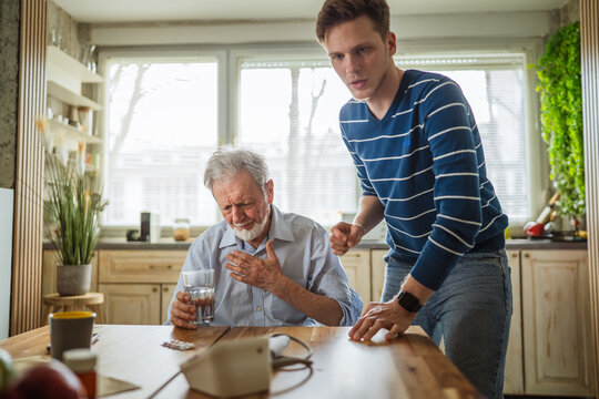 Son helping senior father experiencing chest pain at home