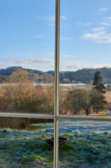 Naklejka premium Window, frame and view of field in countryside with blue sky, trees and outdoor landscape. Background, empty and glass pane with scenery of meadow, environment and nature for season in Denmark