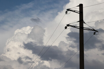 Fototapeta premium Electricity pylon silhouette against dramatic white cumulus clouds
