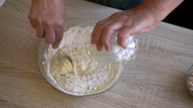 Close up of hands mixing flour and dough in glass bowl on wooden table, pouring liquid from jar, home baking process for cooking tutorials and recipe content