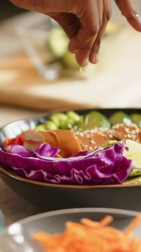 Vertical video: Entering hand sprinkling sesame, finishing poke bowl on counter with wooden bowl