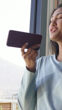 Vertical video: Raising Asian woman holding phone to mouth by balcony, recording song, blue shirt