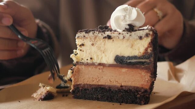 Close up motion of person taking a bite of delicious cheesecake with chocolate and cookies and cream layers with whipped cream topping