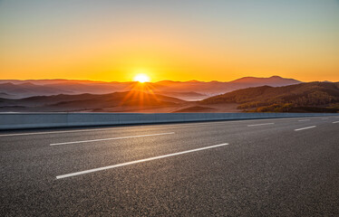 Empty asphalt highway through dramatic mountain landscape at sunrise, transportation and logistics concept, copy space.