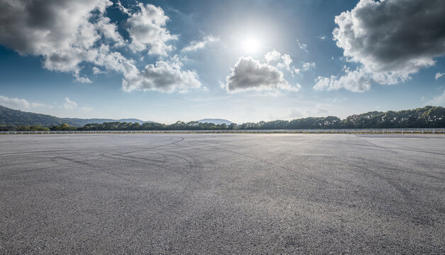 Large empty asphalt parking lot with tire marks under blue sky for commercial display.