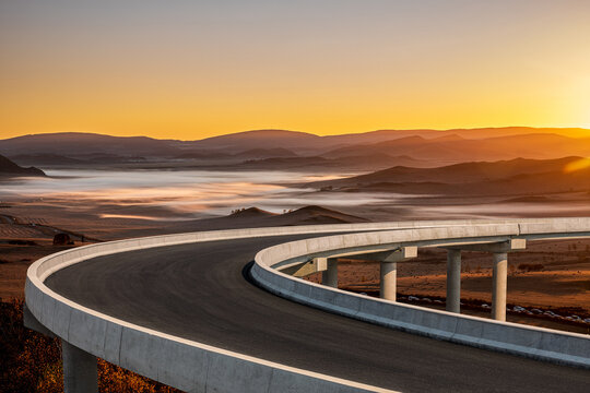 Curved concrete highway bridge overpass overlooking a misty valley landscape during a beautiful golden sunset in China.