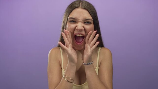 Caucasian teenage girl covers mouth with hands and opens her eyes wide to reveal bare shoulders in purple studio; surprise.
