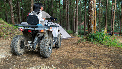 Fototapeta premium a young boy and girl riding an all-terrain vehicle (ATV) along a dirt path in a lush pine forest.
