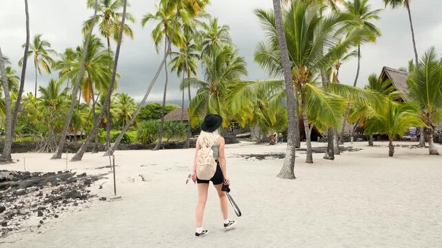 Beautiful girl walking around palm trees inside exotic Puuhonua O Honaunau National Historical Park in Big Island, Hawaii. High quality 4k footage