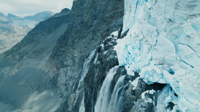 Melting glacier forming majestic waterfalls down rugged mountainside, cinematic aerial view