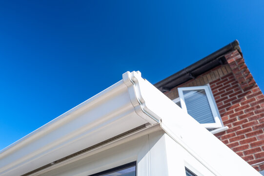 Close-up of white plastic guttering seen on a conservatory which extends from the main house. Seen with newly replacement PVC window.