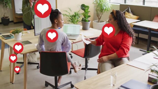 Woman in red handing sheet and sparking animated hearts, colleague reaching laptop across business