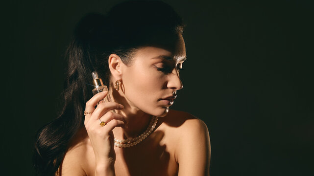 Woman applying serum with dropper bottle in moody lighting studio portrait. Concept of skincare routine, cosmetic application, beauty care and premium product advertising.
