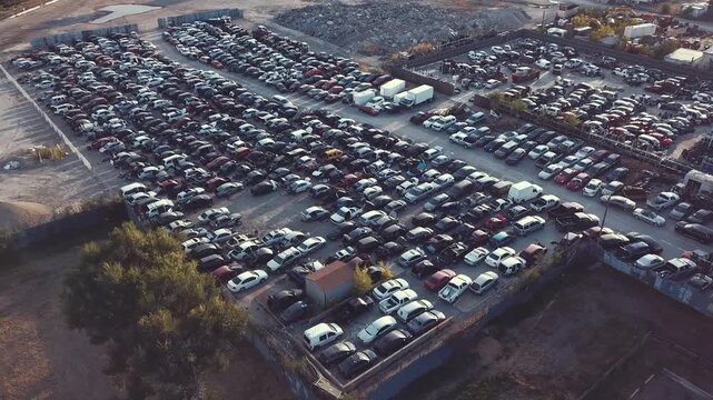 Aerial drone shot over large auto salvage yard with rows of wrecked cars, showing damaged vehicles for recycling or parts, industrial scene