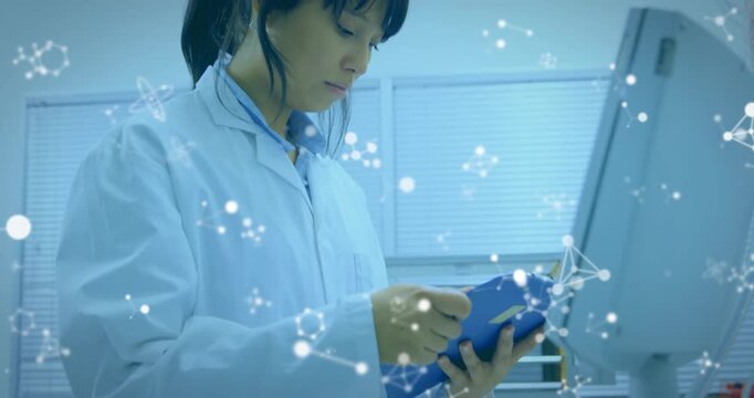 Lab tech tapping blue tablet reviewing data showing network graphics on monitor camera pulling back
