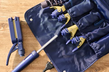 Fototapeten Friseursalon Tools and equipment for hairstyling are arranged on a wooden surface beside a case holding curling rods  © mira_y