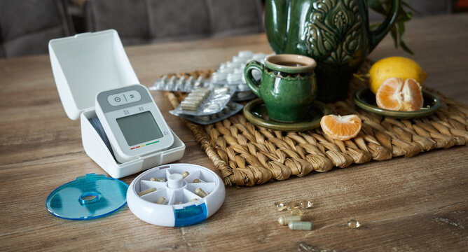 Home health setup with medication organizer, blood pressure monitor, and drink on wooden table