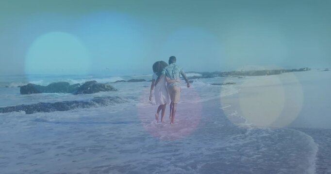 Walking couple, waves lapping, holding and stepping through surf to rocks dress print shirt bokeh