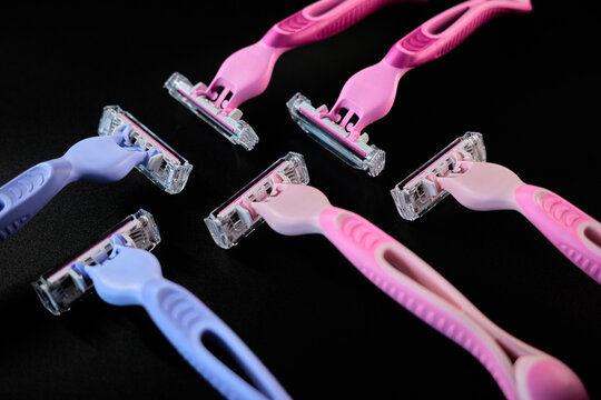 Various razors in different colors laid out on a black surface in a simple arrangement