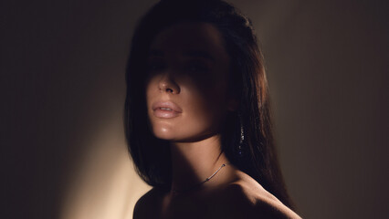 Fototapeta premium Low key portrait of woman with shadow across face in studio lighting. Concept of fashion branding, beauty campaign visuals, cosmetic advertising and luxury style promotion.