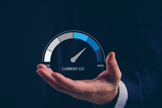 Businessman hand holding virtual current CCI gauge indicating high performance business measurement concept dark background.