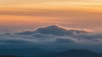 Fototapeta premium Sunset over mountain peaks with layered clouds and warm sky hues