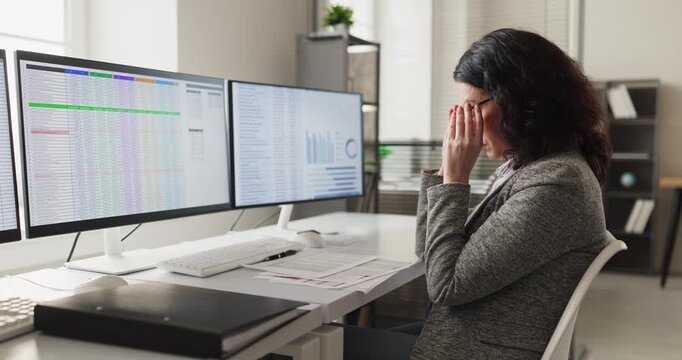 Woman office worker with stress and headache. Massages temples by computer screens with data and analysis, feeling fatigue from long hours and deadlines. Clear concept of stress and burnout.