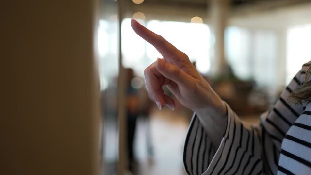Close-up of a female customer's hand using a smartphone for contactless payment, then touching and swiping on an interactive digital screen for self-service in a bright, modern setting