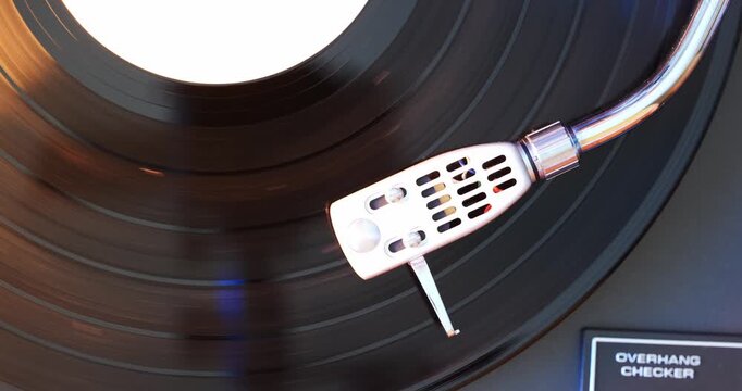 Turntable headshell and needle on a spinning vinyl record. Top down, orange highlight, close up view, no people