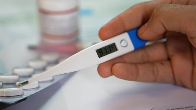 Digital thermometer showing fever with medicine in background
