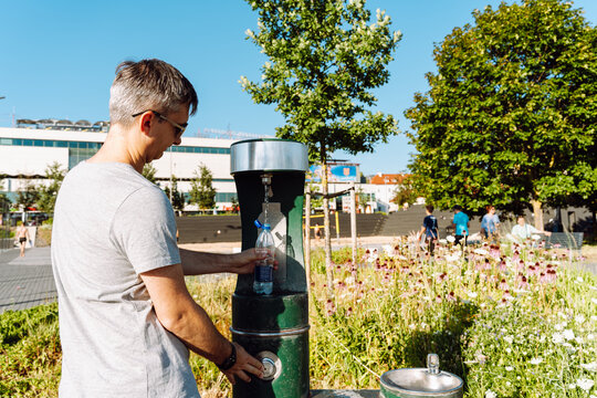 Man filling water bottle at public drinking fountain outdoors