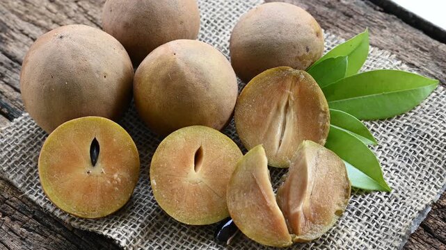Fresh sapodilla (chikoo) fruit cut in half with green leaves on wooden backgrounds