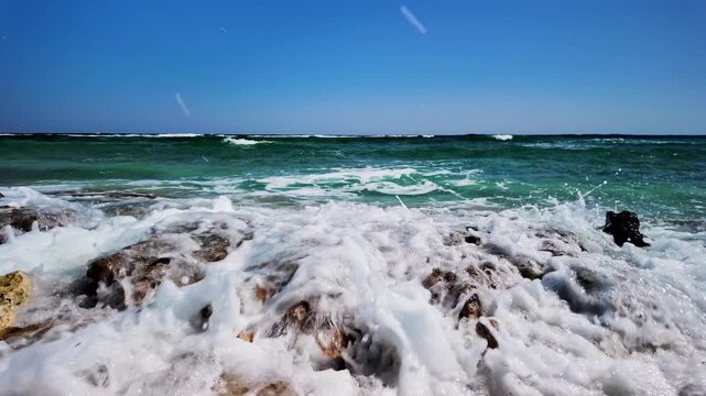 Foamy waves crash against the rocky shore of the Red Sea coast, on a sunny day, near Marsa Alam, Egypt, Africa