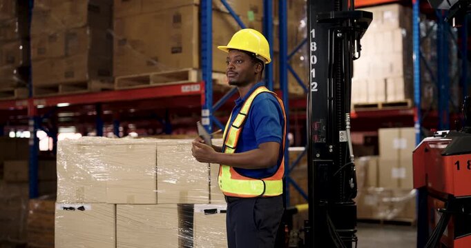 african american male warehouse staff in helmet and safety vest using tablet during stock control pointing to boxes while managing inventory process inside logistic distribution storage center