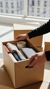 Organizing personal belongings in cardboard boxes for moving or storage. A relatable scene for lifestyle, home, and decluttering themes.