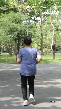 Back view of an elderly Asian woman power walking for exercise in a public park during the morning.