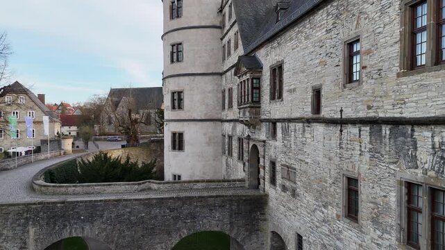 Drone tilts down along the entrance wall showing bridge tower and gateway from an upper perspective.