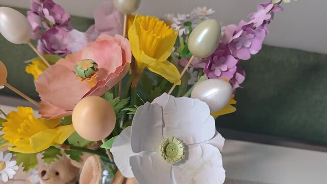 Colorful floral arrangement with decorative eggs and plush bunny dolls on a table, showcasing vibrant spring elements in a cozy indoor setting