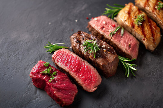 Different cuts of beef steak are arranged on a black surface