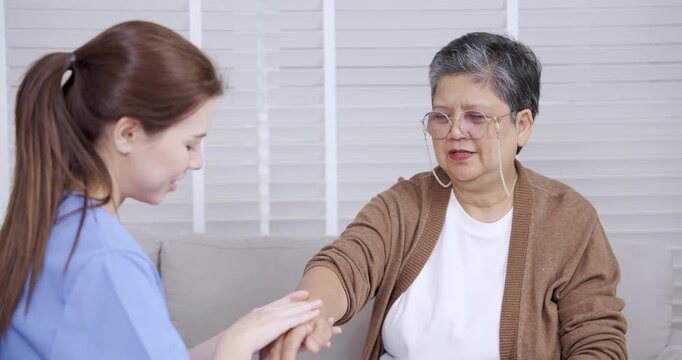 Asian senior female wincing slightly during physical therapy as Caucasian young female physiotherapist assists in examining arm movement and joint flexibility for upper limb rehabilitation