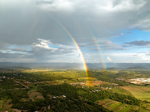 Aerial view of a vibrant double rainbow arching over the sprawling green landscape, painting the horizon with ethereal light, Chilanga, Lusaka Province, Zambia.