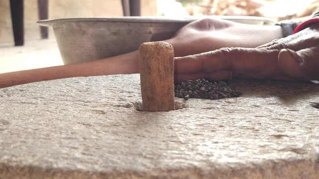 Close-up of a Indian woman using a traditional stone grinder to process grains or spices by hand. This authentic rural scene highlights Indian culture, handmade food preparation