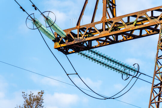 View of a towering rusty metal lattice structure supporting a series of glass insulators and thick cables against a bright blue sky, Kyiv, Kyiv city, Ukraine.