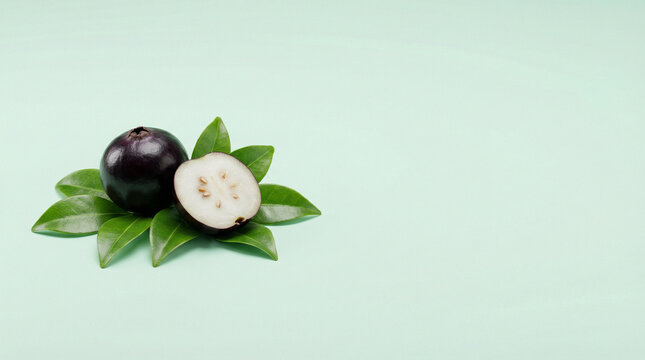 Fresh whole and halved black sapote fruit with green leaves on white background