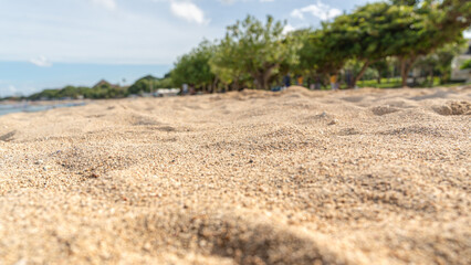 Close up of coarse beach sand texture with blurred tropical trees and blue sky background on a sunny day © Andik