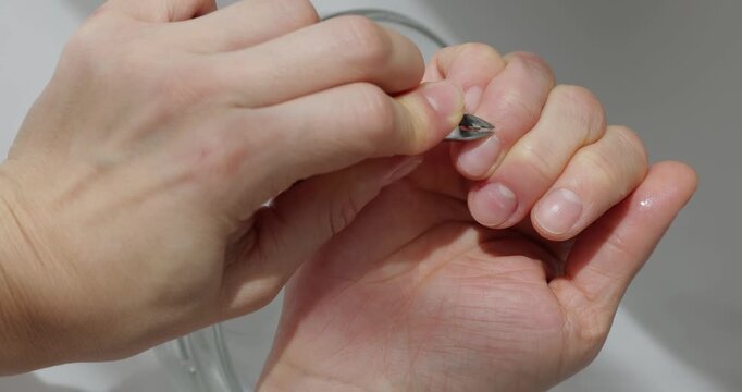Close up of a woman's hands trimming cuticles with nippers over a bowl of water on white background
