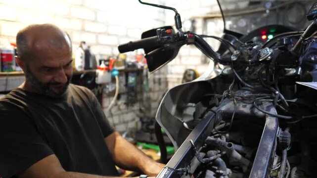 Male mechanic repairing motor of motorcycle at workshop. Adult repairman fixing vehicle engine at workplace. Professional repairer working at garage. Concept of maintenance service. Slow motion