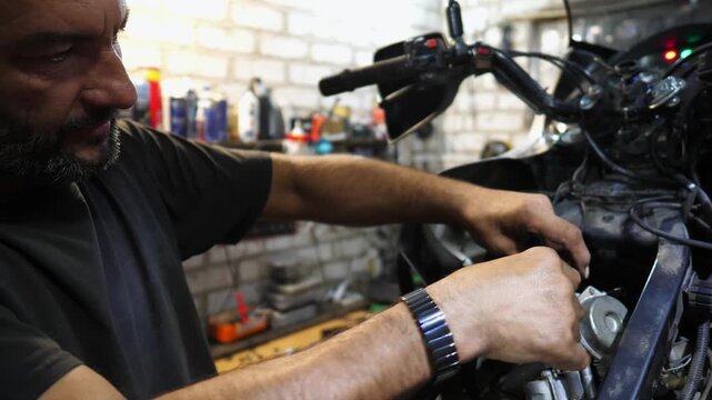 Male repairer fixing motor of motorbike using tool at workplace. Professional mechanic repairing engine of motorcycle at workshop. Adult repairman working at garage. Concept of maintenance service